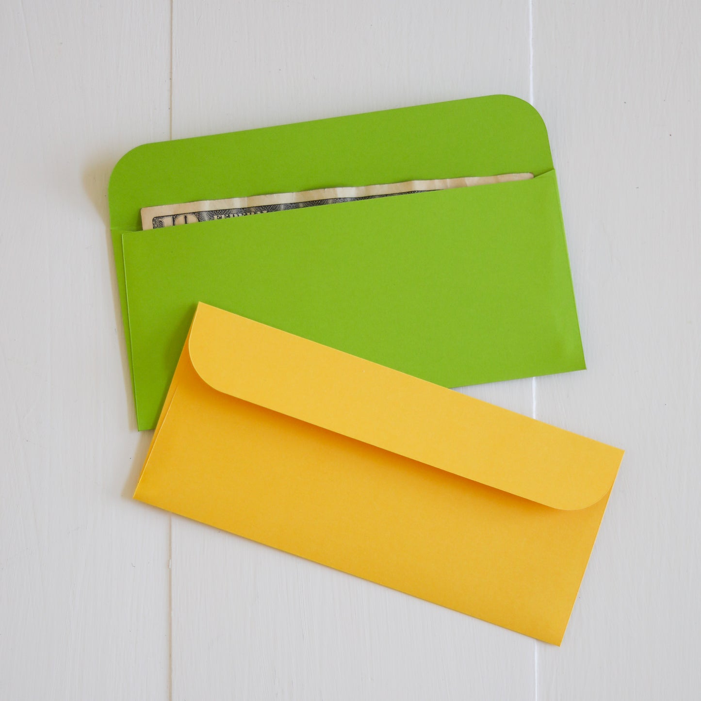 Two envelopes, one green and one yellow, on a light wooden surface.