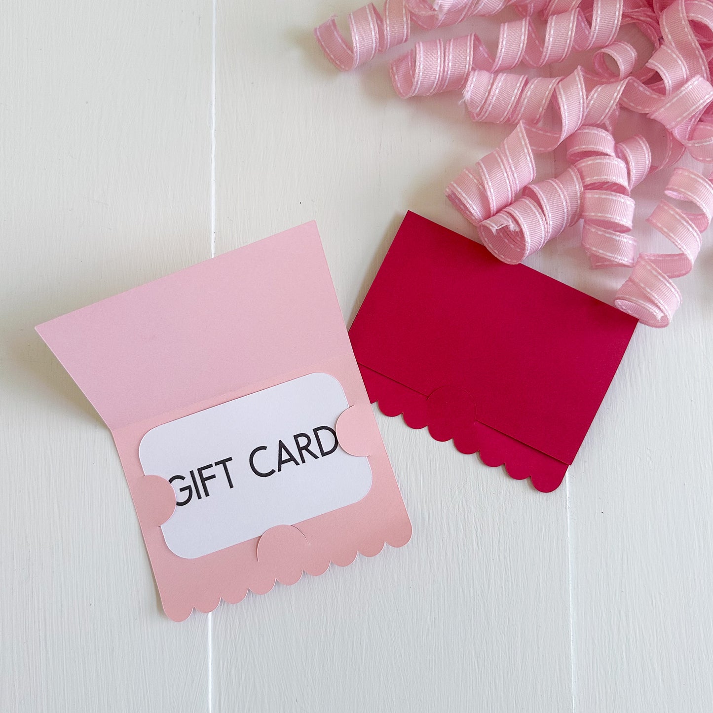 Pink gift card holder with a white card inside, on a light wooden surface with pink ribbons.