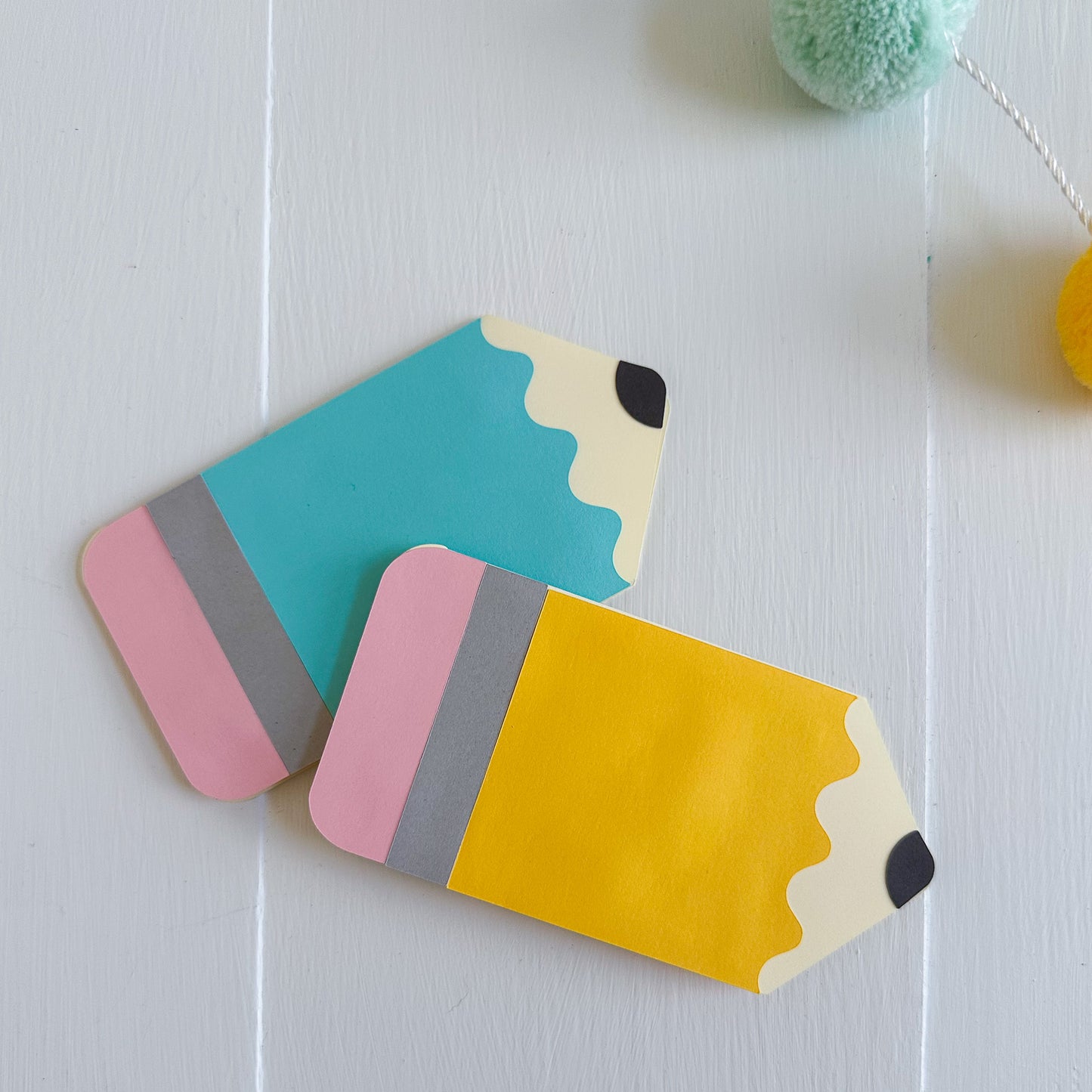 Two colorful pencil-shaped gift card holders on a white surface.