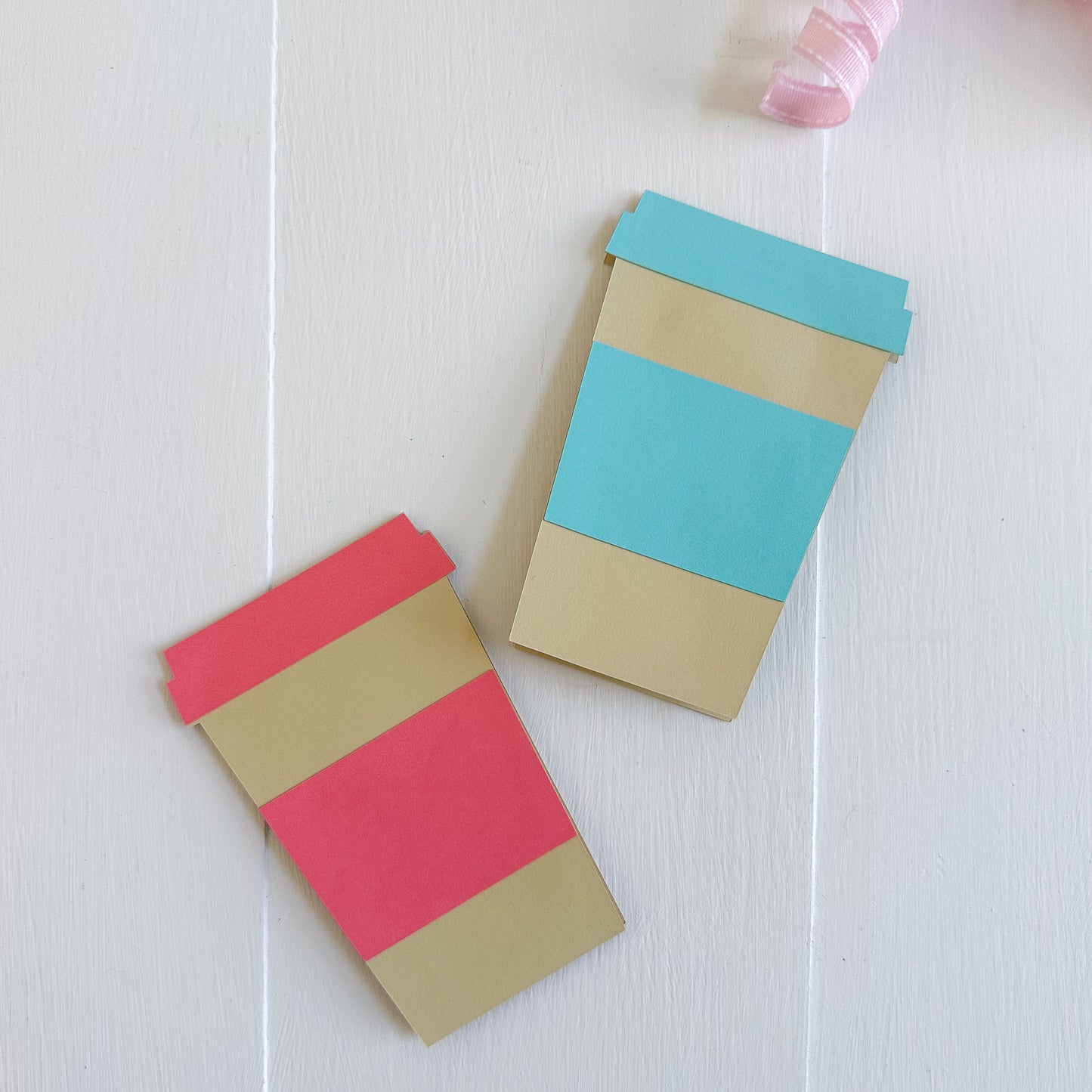 Two colorful paper coffee cup gift card holders on a white surface