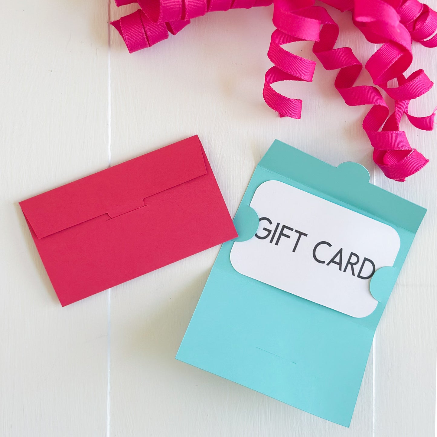 Red envelope and turquoise gift card holder with 'Gift Card' label on a white background with pink ribbons.