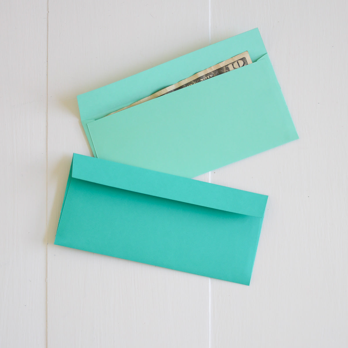 Two turquoise envelopes on a light wooden surface