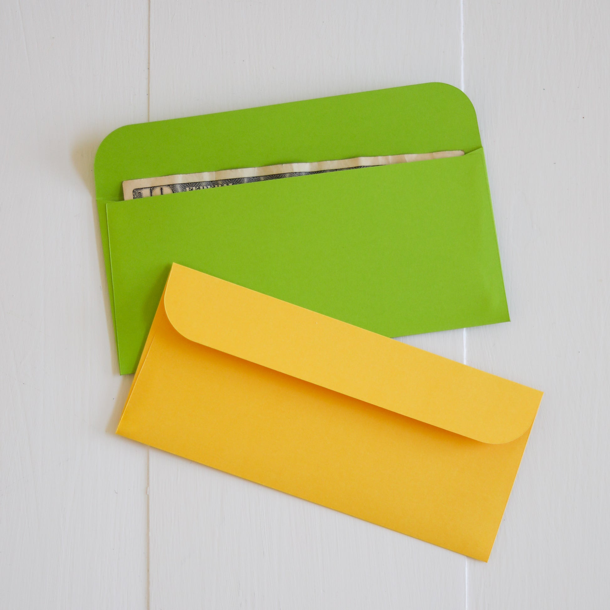 Two envelopes, one green and one yellow, on a light wooden surface.