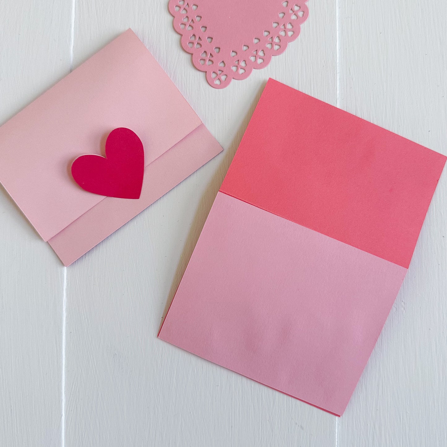 Pink and red gift card holder with a heart-shaped cutout on a white wooden surface