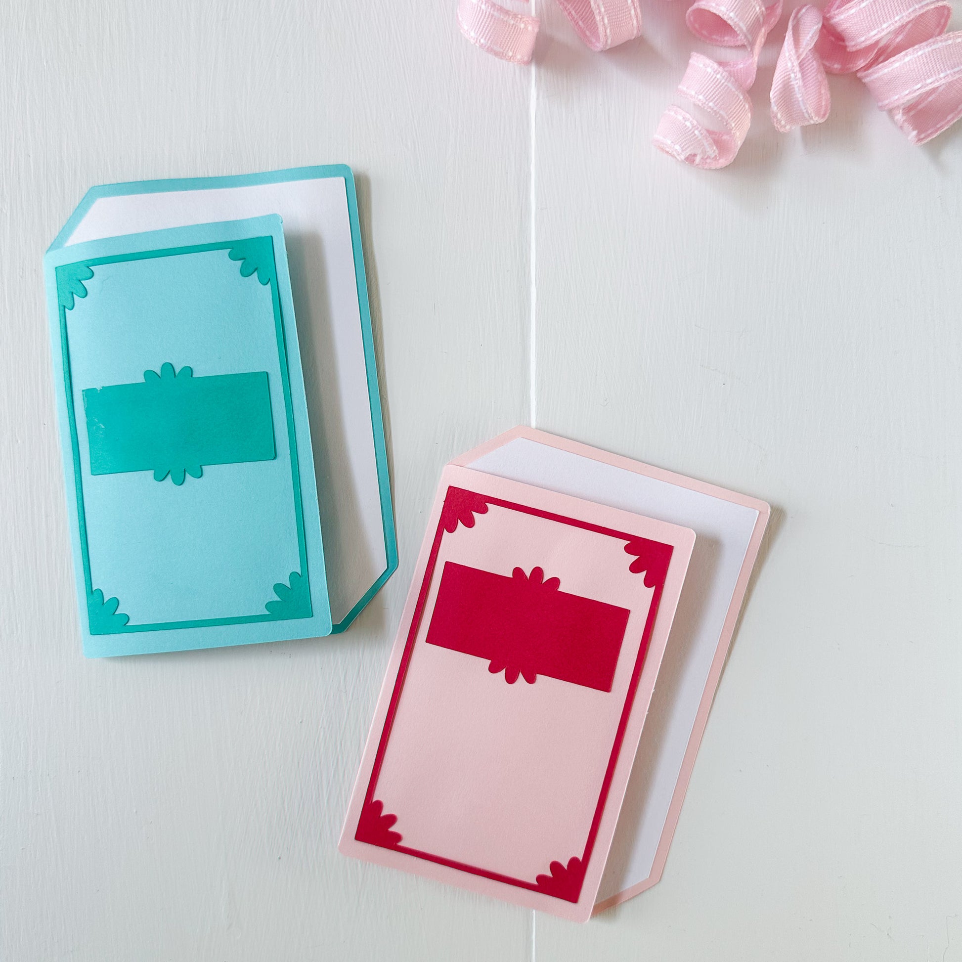 Two colorful book-themed gift card holders on a light surface with pink ribbons.