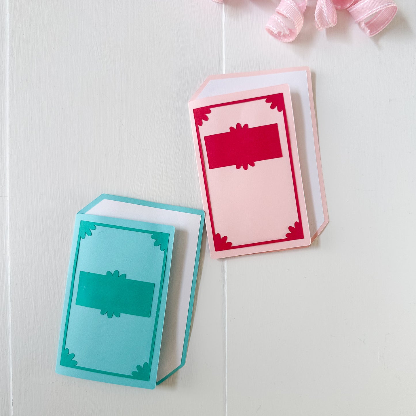 Two colorful book gift card holders on a white wooden surface with pink ribbons.