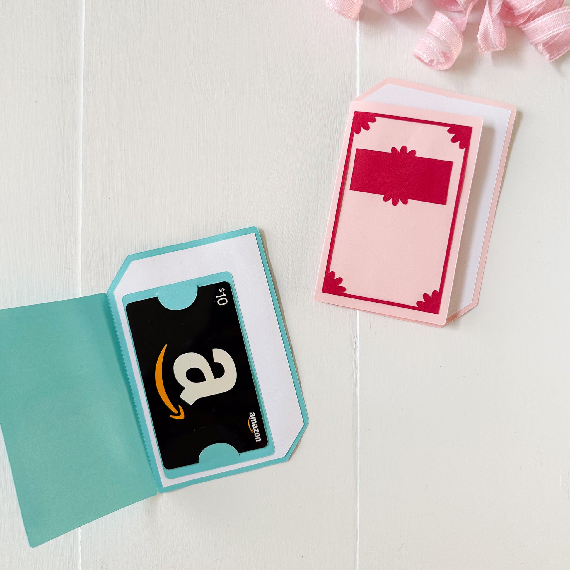 Amazon gift card in a teal book themed gift card holder with a pink book on a white background