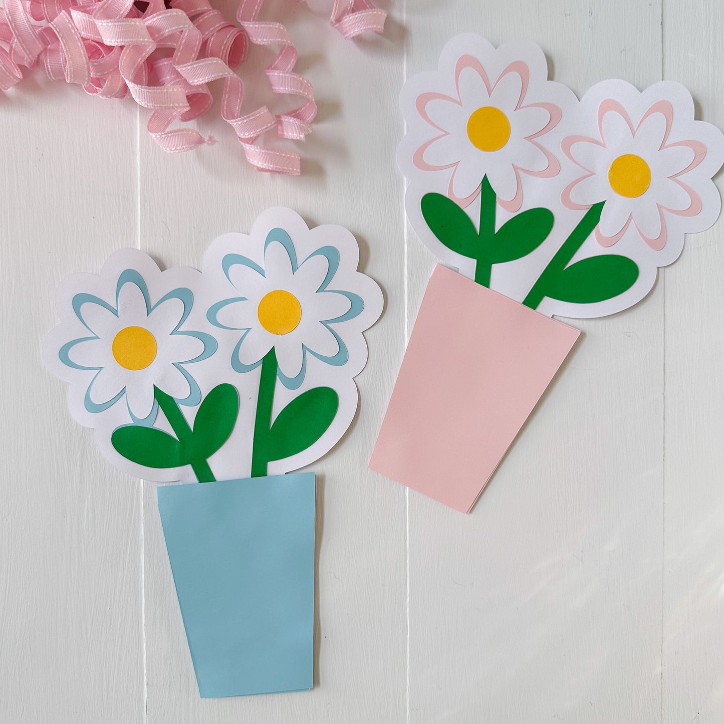 Paper flower gift card holders and a pink bow on a light wooden surface