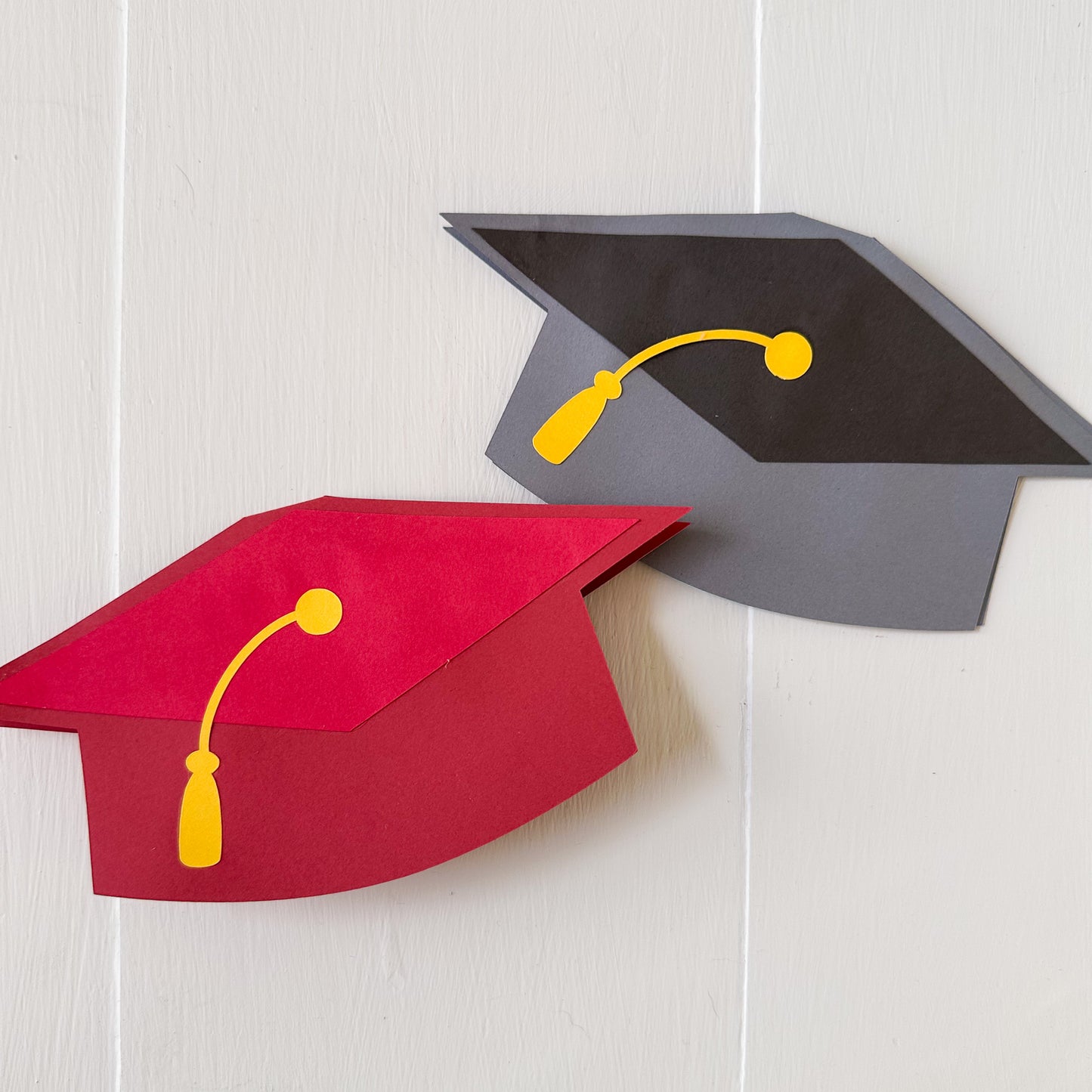 Red and gray graduation cap gift card holders with yellow tassels on a white background