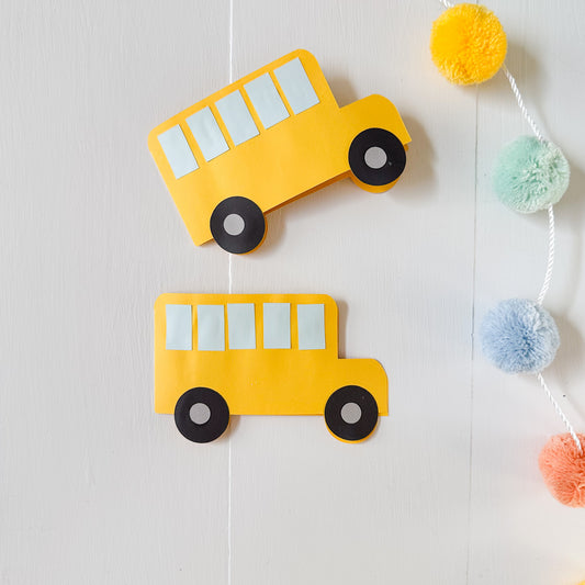 Two yellow school bus-shaped gift card holders on a white wall with colorful pom-poms.