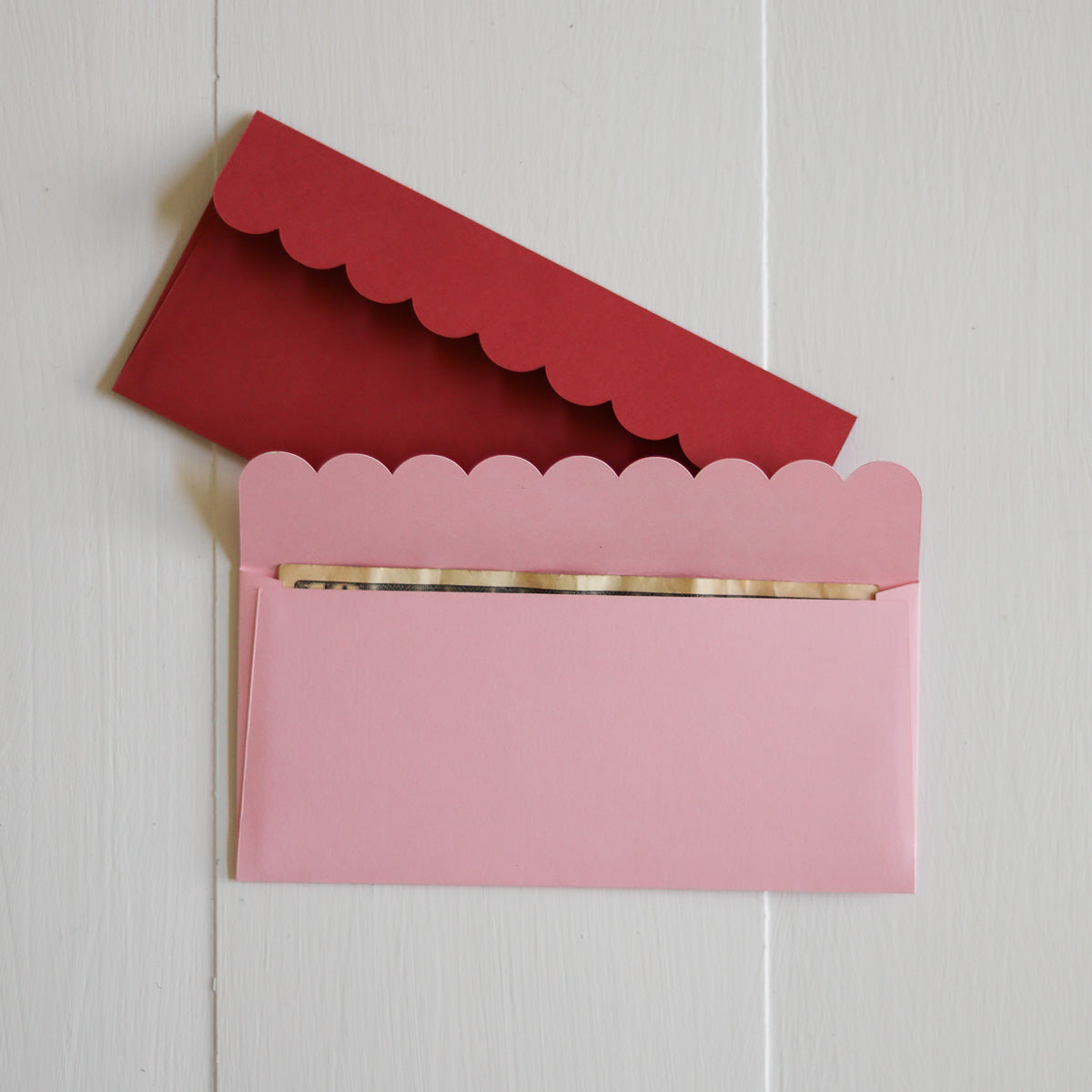 Pink envelope with scalloped edges on a white wooden surface